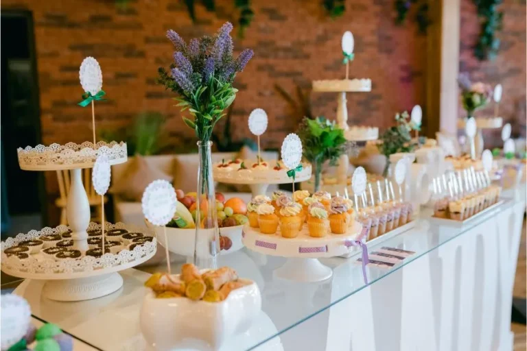 Elegante mesa de candy bars para evento, con dulces, cupcakes y decoración floral.