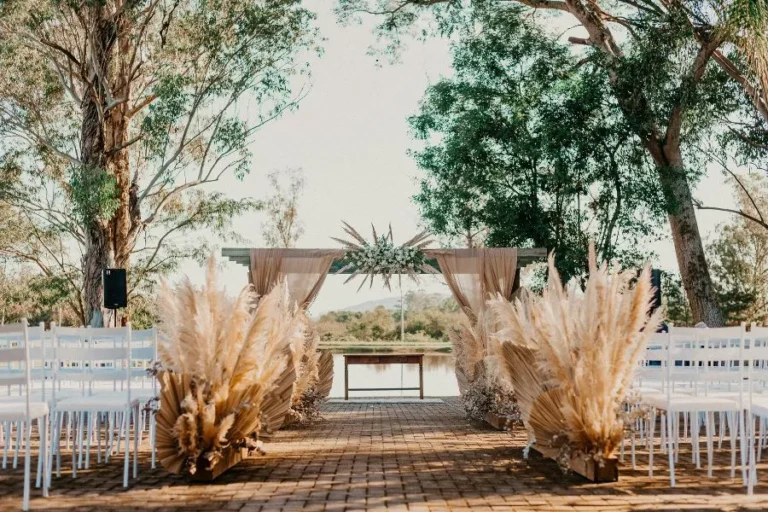 Decoraciones en bodas al aire libre con flores secas, sillas blancas y un altar elegante frente al lago.