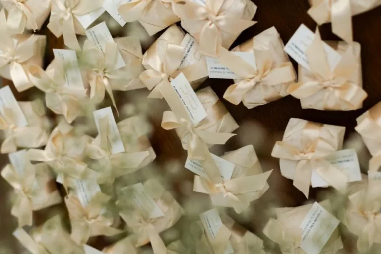 Pequeños regalos de boda para invitados envueltos con elegancia en cintas crema y tarjetas personalizadas.