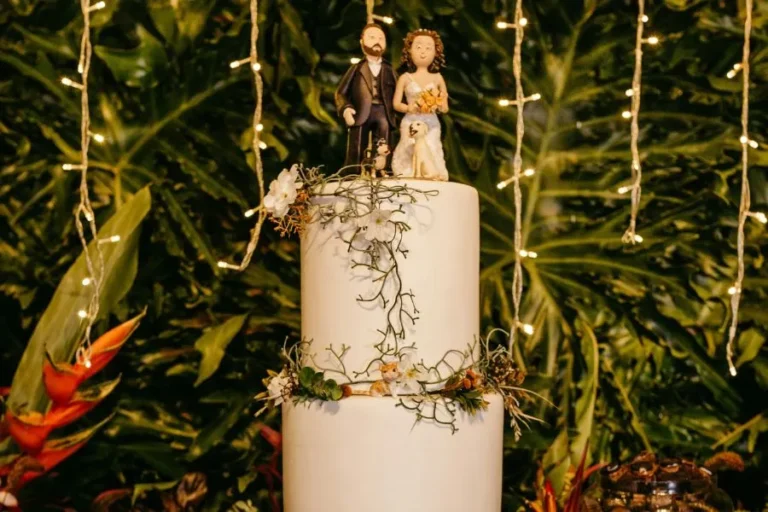 Figuras de novios encima de una tarta de dos pisos blanca con un fondo de selva